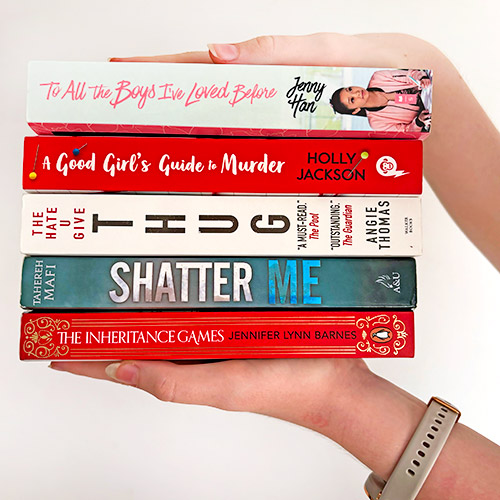 Hands holding a stack of young adult books